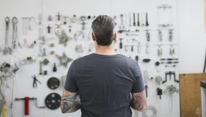 Tattooed helicopter mechanic looking at tools on wall